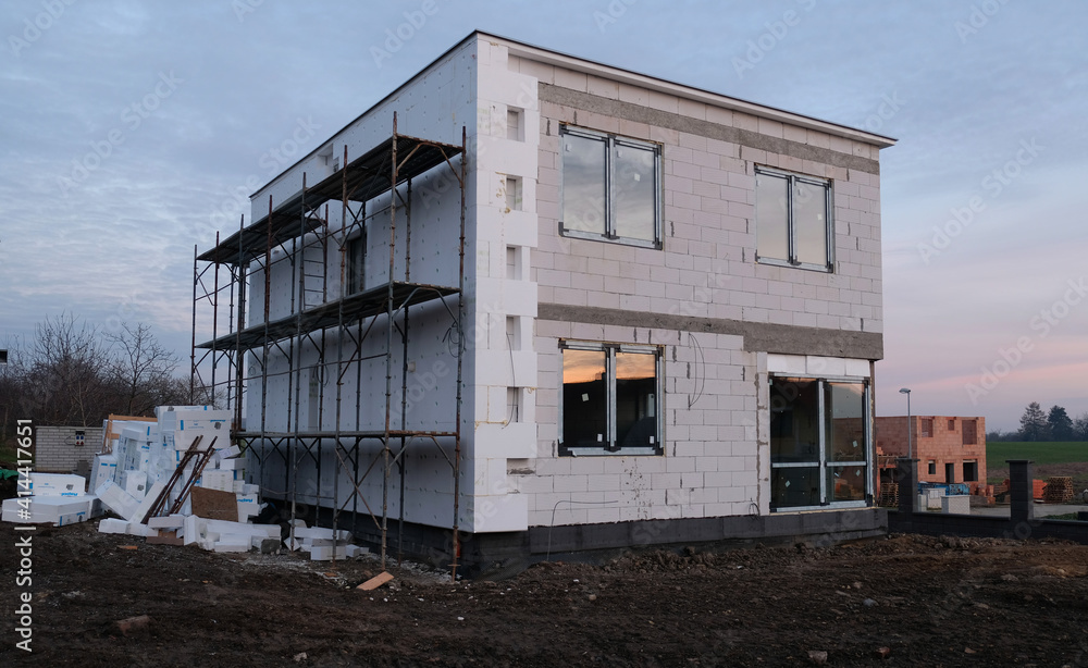 View of an unfinished two-storey house, typical modern suburban house construction. Partially built house. Construction site, incomplete construction and garbage. Insulation of facade to save energy. View of an unfinished two-storey house, typical modern suburban house construction. Partially built house. Construction site, incomplete construction and garbage. Insulation of facade to save energy.