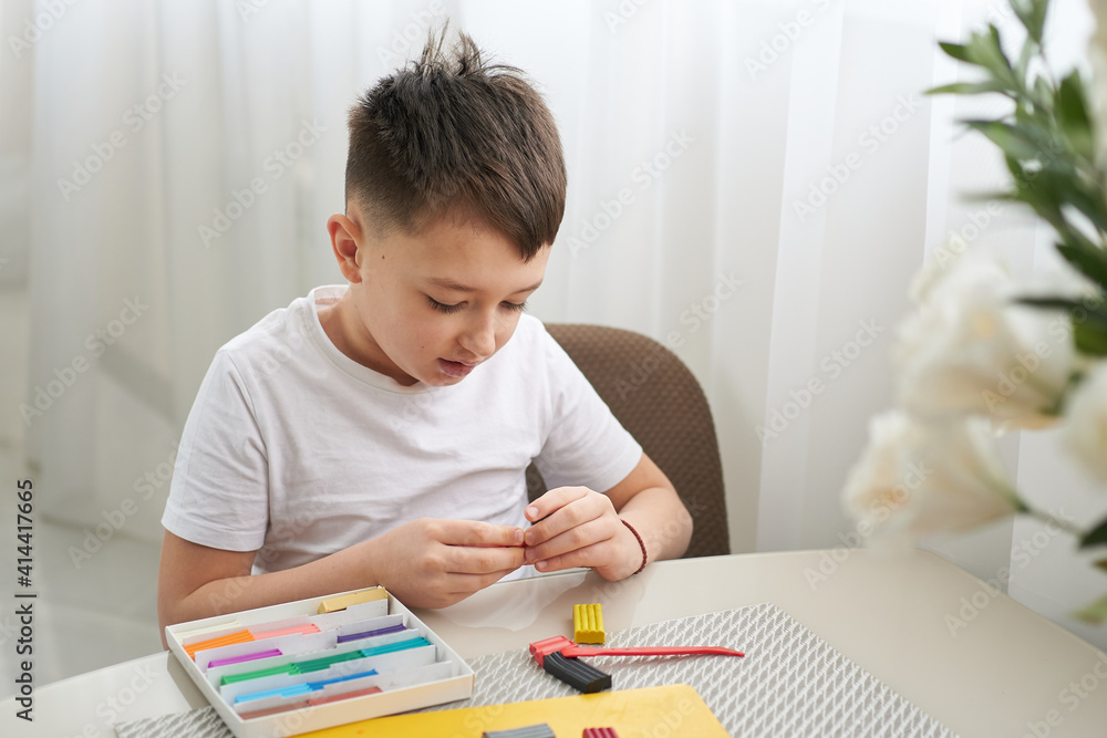 boy sculpts figures from plasticine, sitting at home at the table. He is passionate about his hobby boy sculpts figures from plasticine, sitting at home at the table. He is passionate about his hobby