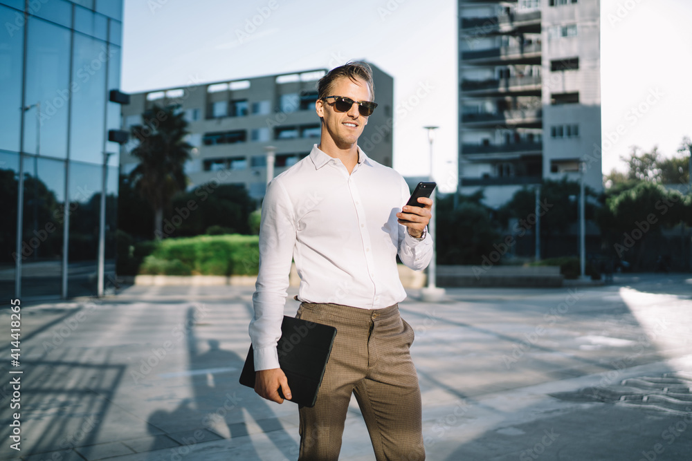 Half length portrait of trendy dressed businessman in stylish clothing using modern cellphone device at urban setting, successful male owner with smartphone and touch pad posing in financial district Half length portrait of trendy dressed businessman in stylish clothing using modern cellphone device at urban setting, successful male owner with smartphone and touch pad posing in financial district