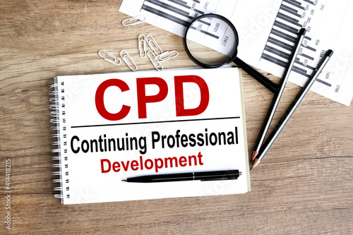 CPD. text on white notepad paper on wood background, near a magnifying glass. photo