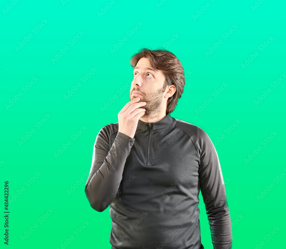 Long haired man is thinking about something, colorful background and sportive clothes. Looking up and aside. He put hand on chin. Long haired man is thinking about something, colorful background and sportive clothes. Looking up and aside. He put hand on chin.