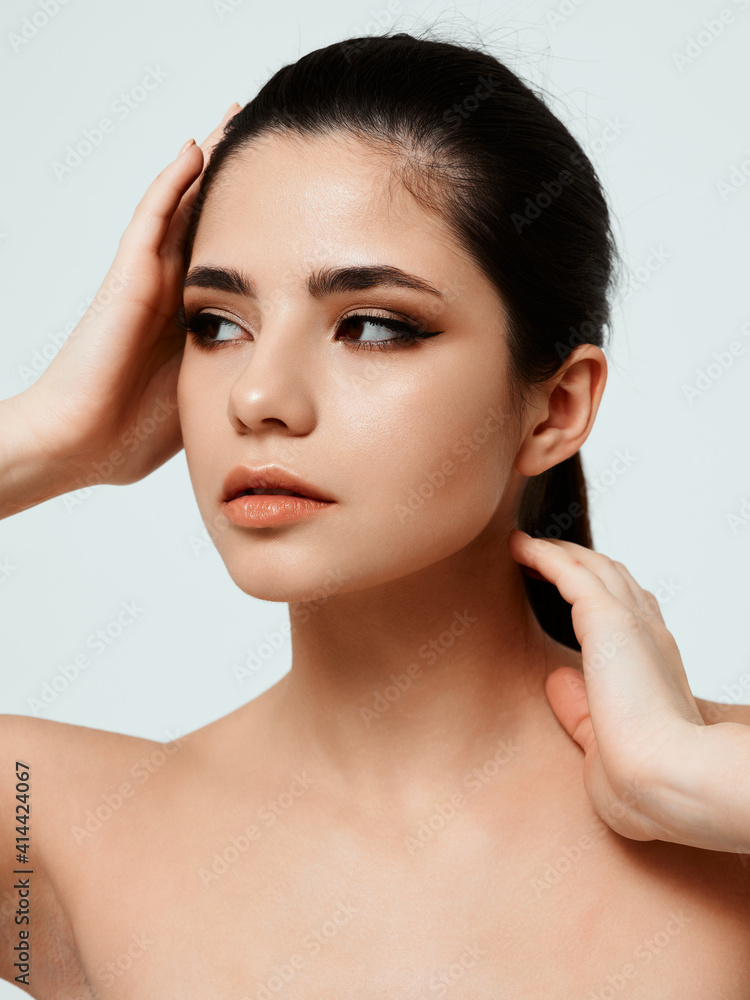 woman with dark hair touching her neck with her hands light background cropped view