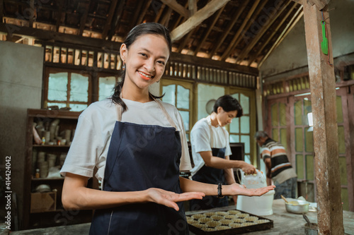 Beautiful employee in apron offering you something from her palms on kitchen background