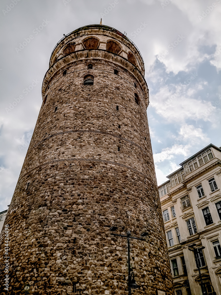 Bottom view of Galata Tower in Istanbul (Turkey), vertical. Old medieval stone high round building against a cloudy sky, close-up