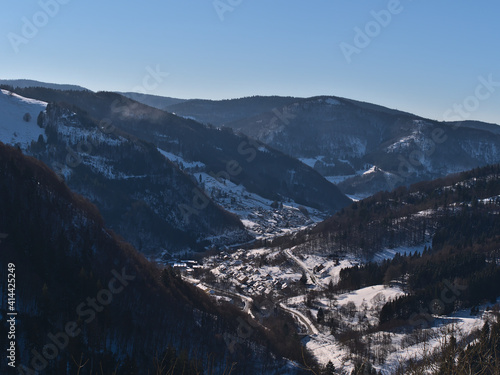 Beautiful aerial view of small village Todtnau, Germany, located in a valley in Black Forest mountain range, in winter season with snow-covered trees on sunny day with blue sky.