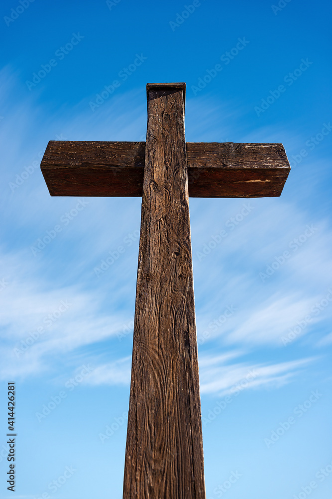 Closeup of a wooden Christian cross on a clear blue sky with clouds and copy space. Garda, Verona province, Veneto, Italy, Europe.