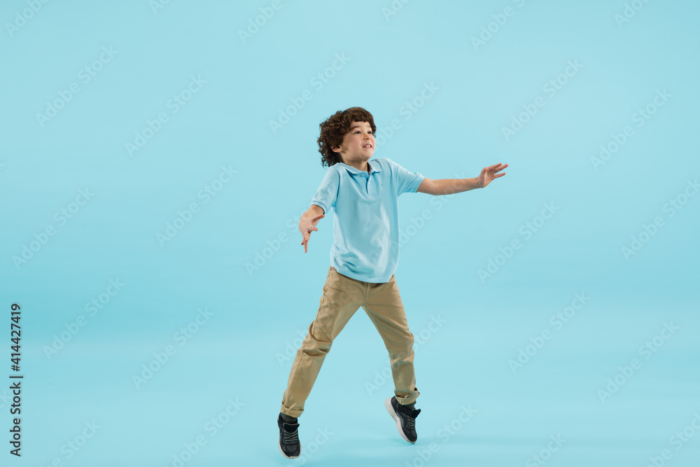 Flying, jumping high. Childhood and dream about big and famous future. Pretty little boy isolated on blue studio background. Dreams, imagination, education, facial expression, emotions concept.
