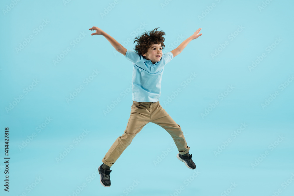 Flying, jumping high. Childhood and dream about big and famous future. Pretty little boy isolated on blue studio background. Dreams, imagination, education, facial expression, emotions concept. Flying, jumping high. Childhood and dream about big and famous future. Pretty little boy isolated on blue studio background. Dreams, imagination, education, facial expression, emotions concept.