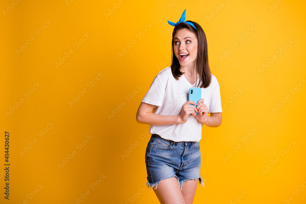Photo portrait of surprised girl keeping mobile phone looking at blank space with opened mouth isolated on vivid yellow color background Photo portrait of surprised girl keeping mobile phone looking at blank space with opened mouth isolated on vivid yellow color background