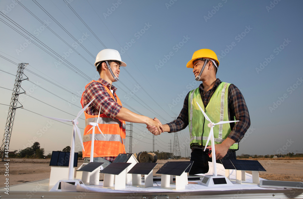 Engineer and construction workers shaking hands together with model of soar project on foreground , new Solar energy generator and village business agreement Engineer and construction workers shaking hands together with model of soar project on foreground , new Solar energy generator and village business agreement