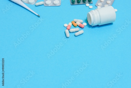 Scattered white pills on blue table.Medical, pharmacy and healthcare concept. Blue background white pills with a medical statoscope, top view.