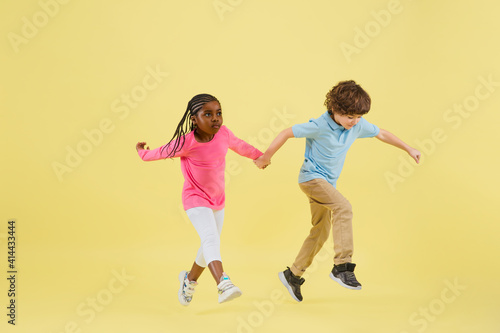 Jumping high. Childhood and dream about big and famous future. Pretty little kids isolated on yellow studio background. Dreams, imagination, education, facial expression, emotions concept.