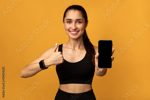 Happy sporty lady showing phone with blank empty screen © Prostock-studio