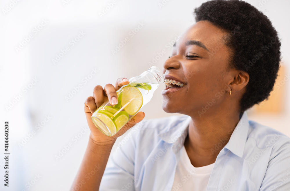 Happy African Woman Drinking Infused Water Posing With Bottle Indoors Happy African Woman Drinking Infused Water Posing With Bottle Indoors