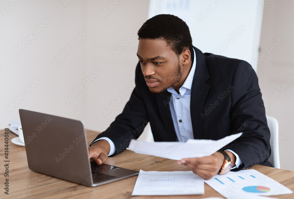 African american manager checking marketing report, using laptop African american manager checking marketing report, using laptop