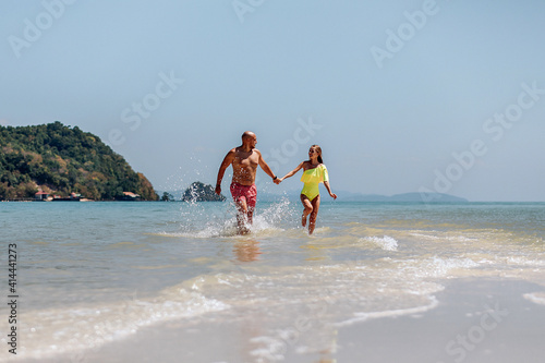 Happy married couple, holding their hands, running along the seashore and spray from the water flying in all directions. Concept of love.