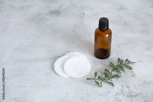 A brown glass bottle, cotton swabs, a green twig on a gray table. Cosmetics concept