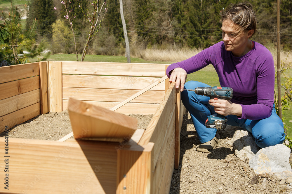 Woman screwing wooden frame for a raised garden bed.