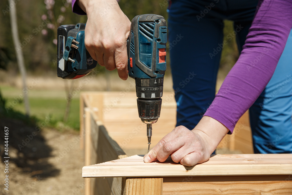 Woman screwing wooden frame for a raised garden bed.