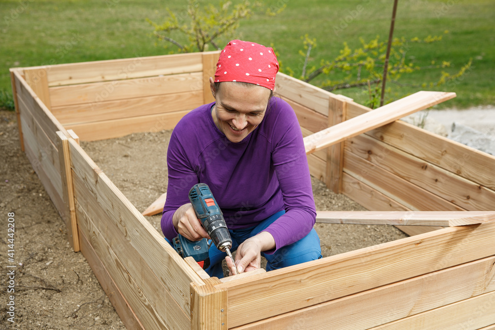 Woman screwing wooden frame for a raised garden bed.