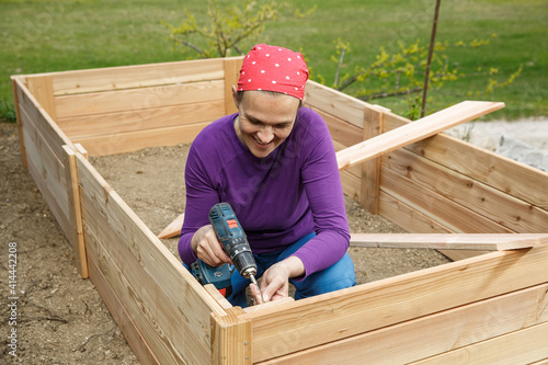 Obraz na płótnie Woman screwing wooden frame for a raised garden bed. w salonie