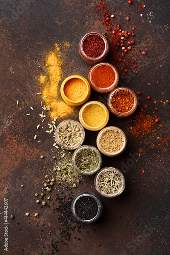 Fototapeta Naklejka Na Ścianę i Meble -  Set of various colorful spices in jars over dark brown concrete background. Assorted condiment. Top view, close up, flat lay. Food background
