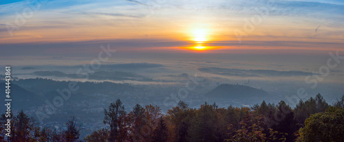 Amazing foggy sunrise over the city of Graz with Schlossberg hill and Church of the Sacred Heart of Jesus tower  in Styria region  Austria. Panoramic view from Plabutsch mountain on autumn morning.