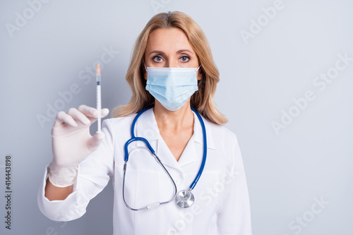 Photo of mature beautiful doctor woman with face mask doing coronavirus vaccination isolated on grey color background