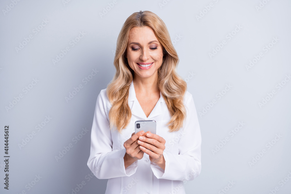 Photo of shiny sweet age woman therapist dressed white coat communicating modern device isolated grey color background Photo of shiny sweet age woman therapist dressed white coat communicating modern device isolated grey color background