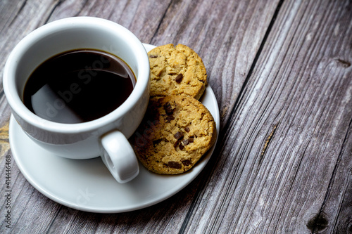 chocolate chip cookies next to a cup of coffee on a saucer on a rustic wooden table