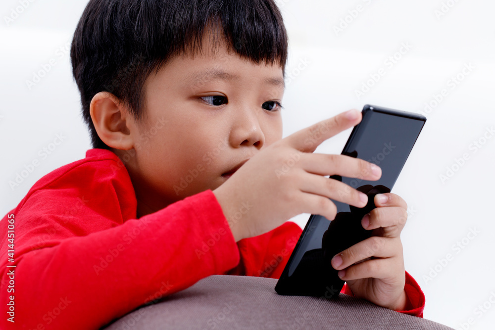 Little Asian boy lying on a pillow enjoying using smartphone at home, isolated on white background. Little Asian boy lying on a pillow enjoying using smartphone at home, isolated on white background.