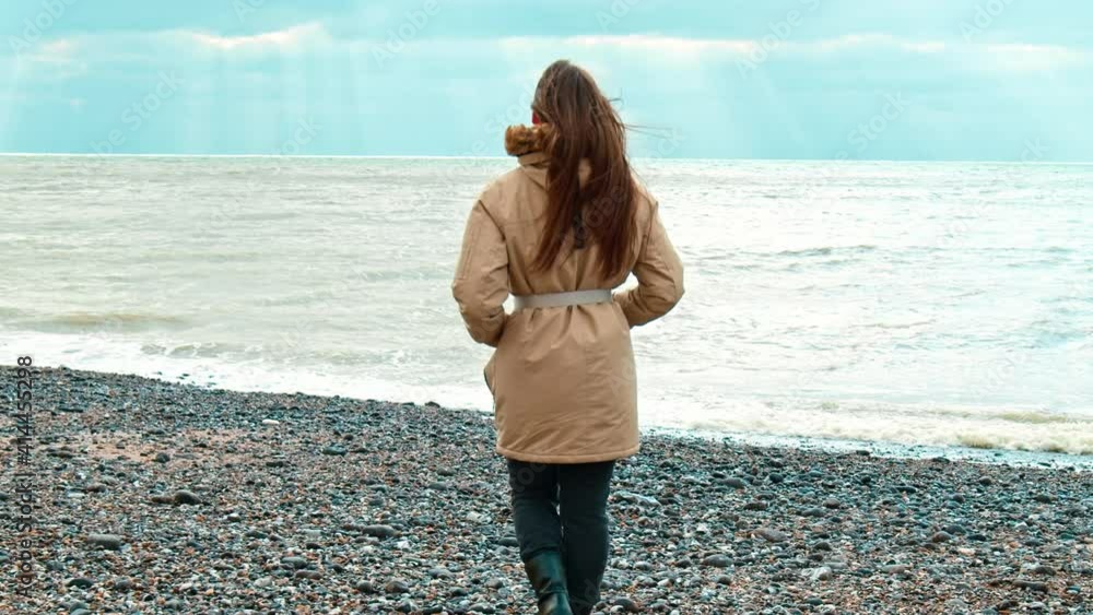 Woman traveller walking in slow motion with toward the sea during winter in 4K. A girl enjoying vacation travel adventure and nature during winter. Woman traveller walking in slow motion with toward the sea during winter in 4K. A girl enjoying vacation travel adventure and nature during winter.