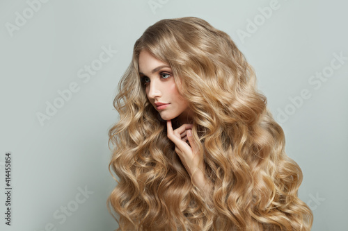 Pretty young blonde woman hair model with long blond healthy curly hairstyle on white background