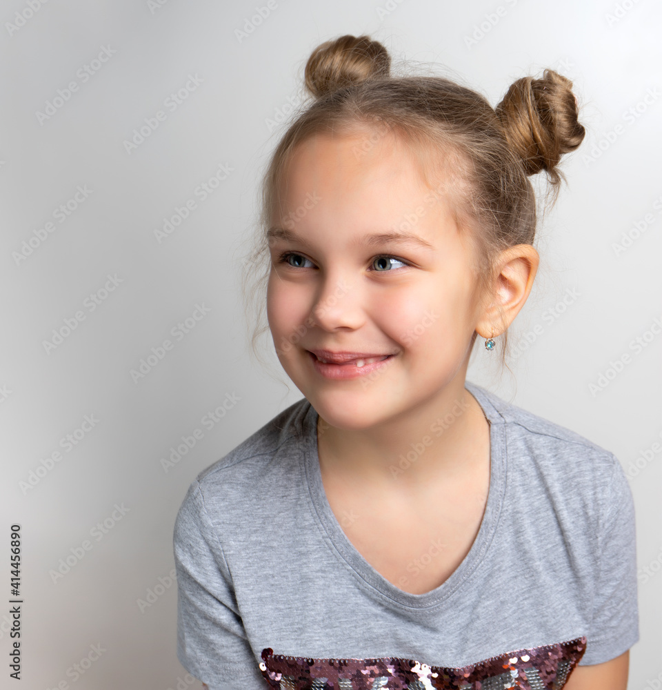 Happy smiling little girl studio headshot portrait isolated on grey background. Beautiful lovely caucasian female child with cute bun hairstyle looking aside. Attractive young model Happy smiling little girl studio headshot portrait isolated on grey background. Beautiful lovely caucasian female child with cute bun hairstyle looking aside. Attractive young model