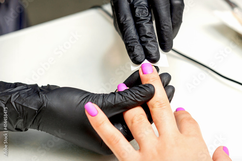 Manicurist applies a matte coating with a napkin on female pink nails in a nail salon