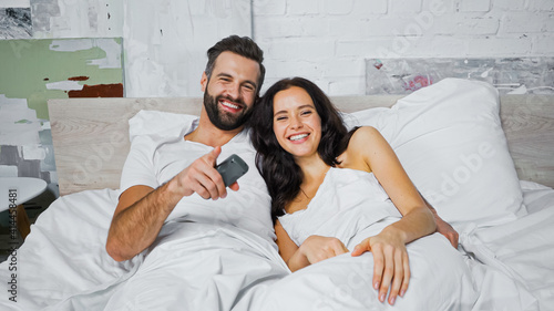 cheerful man pointing with finger while watching tv with girlfriend in bedroom