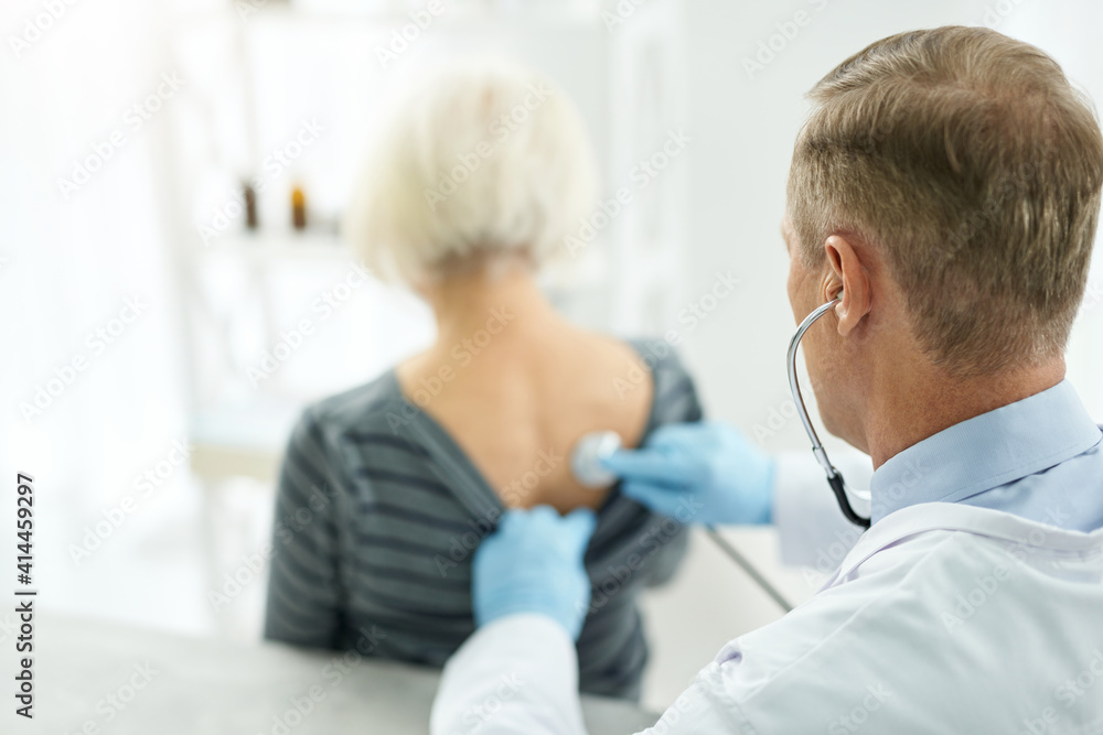 Male doctor examining old woman with stethoscope in clinic Male doctor examining old woman with stethoscope in clinic