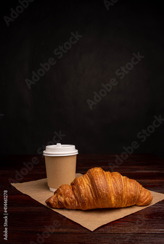 Croissant with coffee to go in a paper cup, take away breakfast