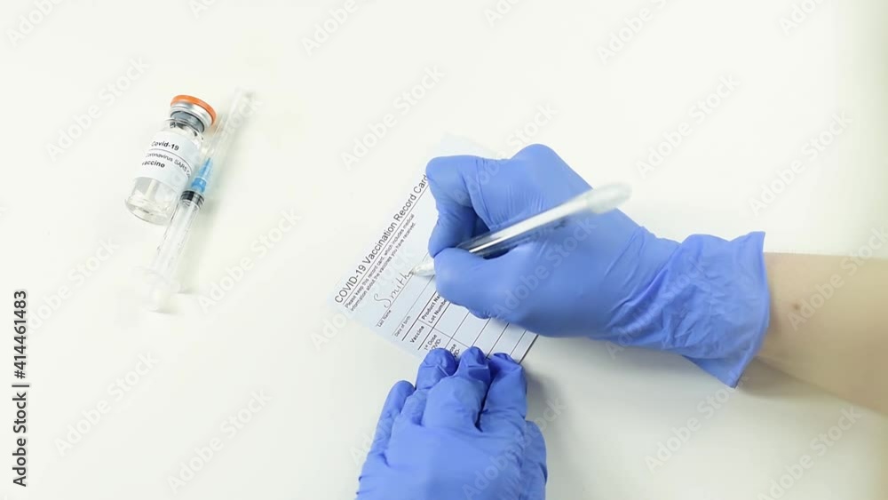 Doctor's hands in medical gloves filling out the vaccination record card, vaccination passport, a vial with covid-19 vaccine and syringe on a white background, close up, copy space. Doctor's hands in medical gloves filling out the vaccination record card, vaccination passport, a vial with covid-19 vaccine and syringe on a white background, close up, copy space.