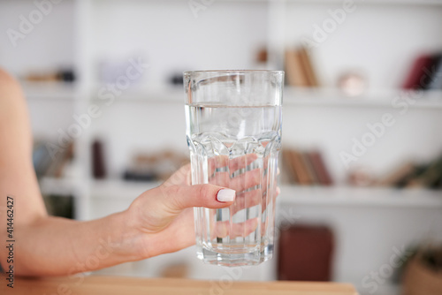 Close-up picture of glass with water in hand of young woman, working at office table, Manager at workplace. Work process in company. Healthy drink consumption concept.Water balance.