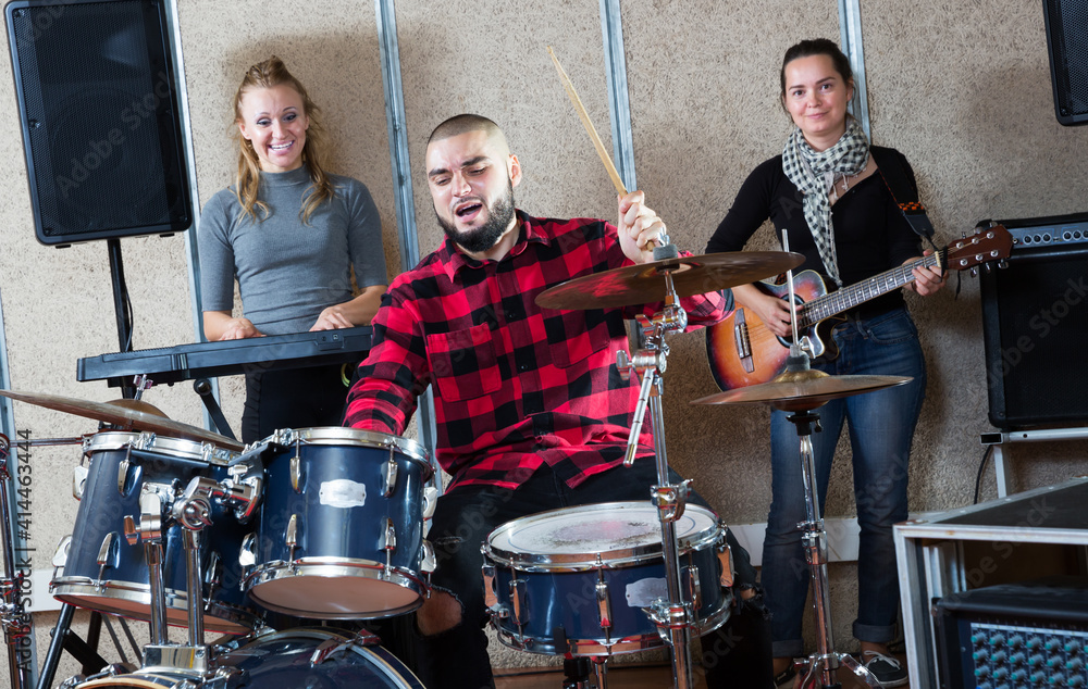 Group of young musicians with expressive male drummer rehearsing in sound studio