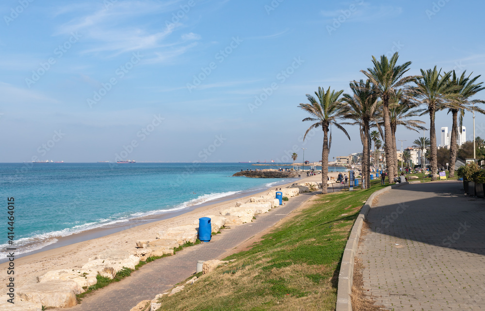 A few tourists and residents of the city walk along the embankment against the backdrop of the Mediterranean Sea in Haifa city, in northern Israel.