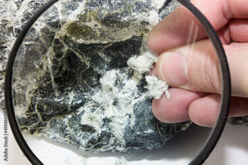 Konstfotografi Hand with magnifying glass examines asbestos fibers in stone.