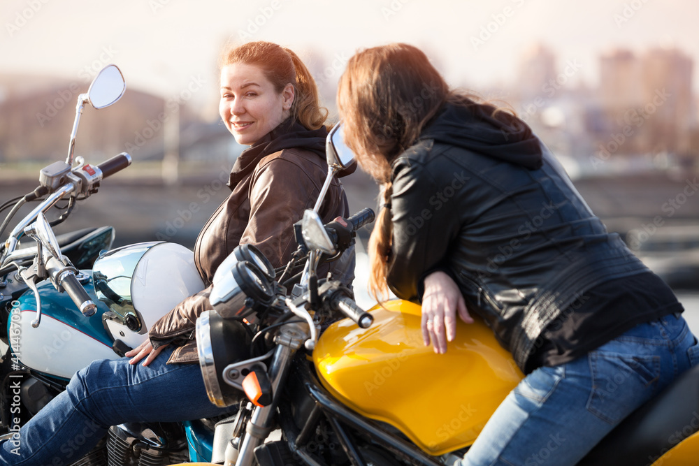 Obraz premium Two European women motorcyclists talking cheerfully while sitting on their motorcycles