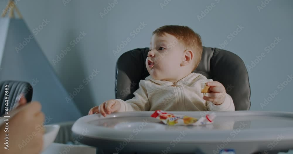 Hungry little boy sitting in a stroller, fed by his mother at home. Slow motion. Hungry little boy sitting in a stroller, fed by his mother at home. Slow motion.