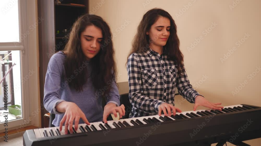 Teenage girls twin sisters at home play electronic piano in four hands during music rehearsal Teenage girls twin sisters at home play electronic piano in four hands during music rehearsal