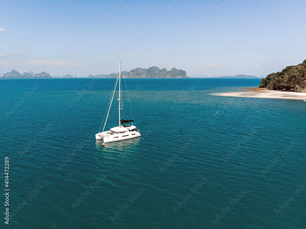 Aerial view of the white luxury yacht floating alone in the exotic turquoise sea near the island filled with forests and at the background of mountains and nature Aerial view of the white luxury yacht floating alone in the exotic turquoise sea near the island filled with forests and at the background of mountains and nature
