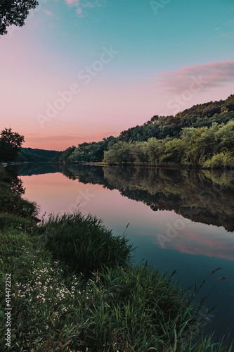 Fototapeta Naklejka Na Ścianę i Meble -  Morning sunrise with pink cotton candy skies and glass like reflections, wildflowers and lush green grass on a summer morning along the Maquoketa River in Iowa, USA.