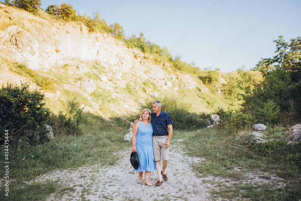 Happy senior man and woman embracing in the park between the rocks. Senior couple walking and having fun in summer