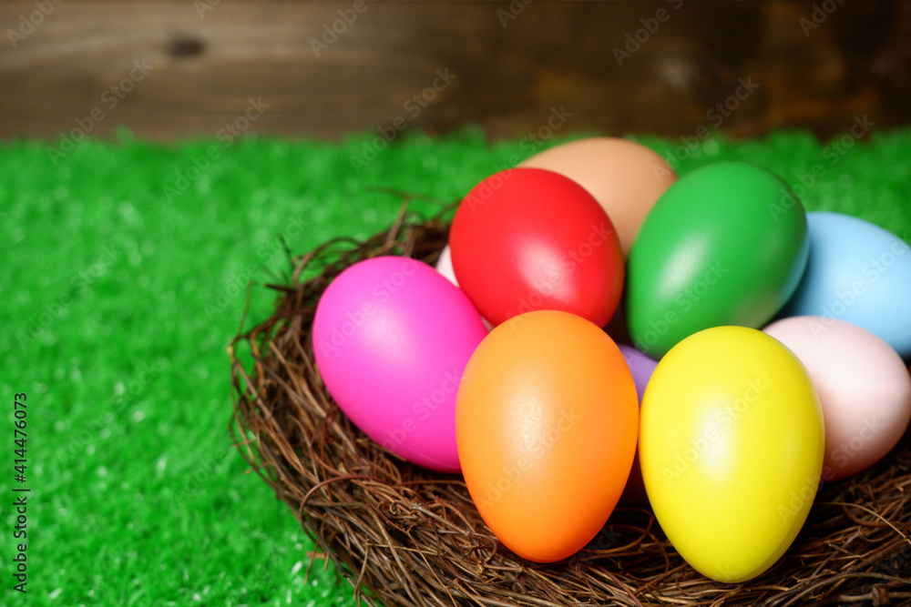 Multi colored easter eggs in birds nest on green grass and wooden panks background closeup view selective focus with copy space. Easter holiday banner, card, poster, voucher, invitation template